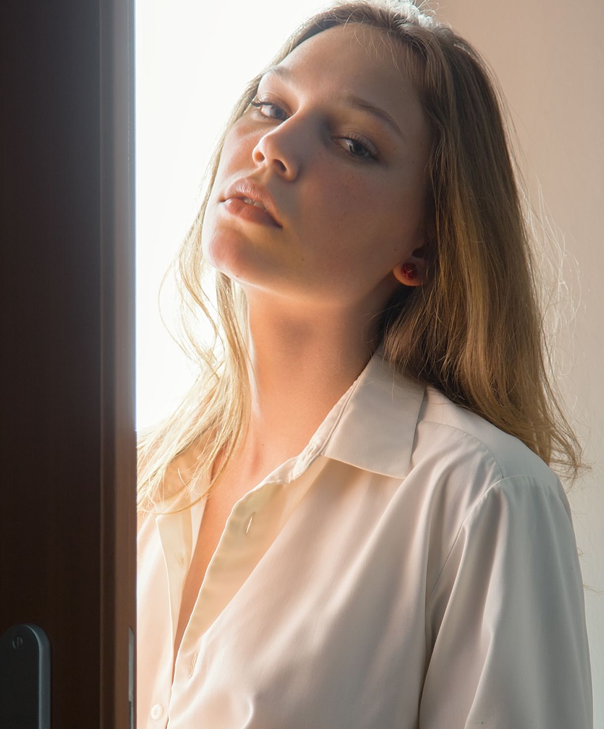 A woman with long, wavy hair wearing a light-colored button-up shirt, leaning slightly towards the camera with a contemplative expression.