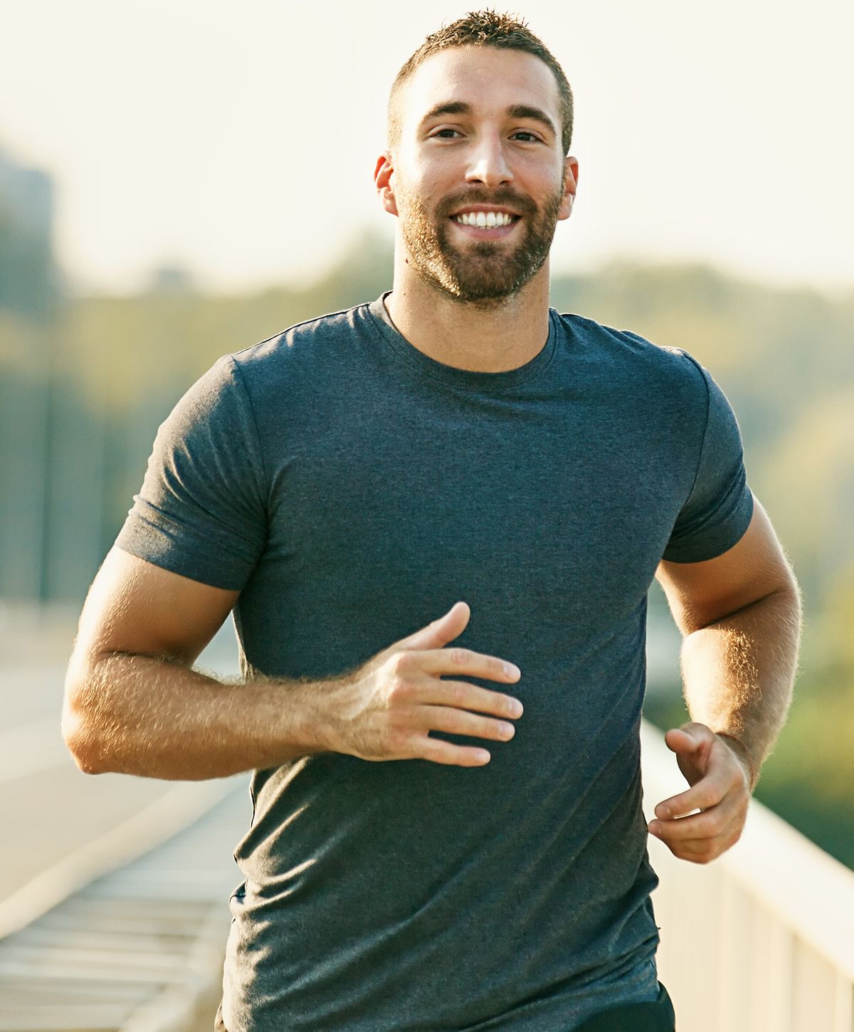 A smiling man in a gray t-shirt jogging outdoors.