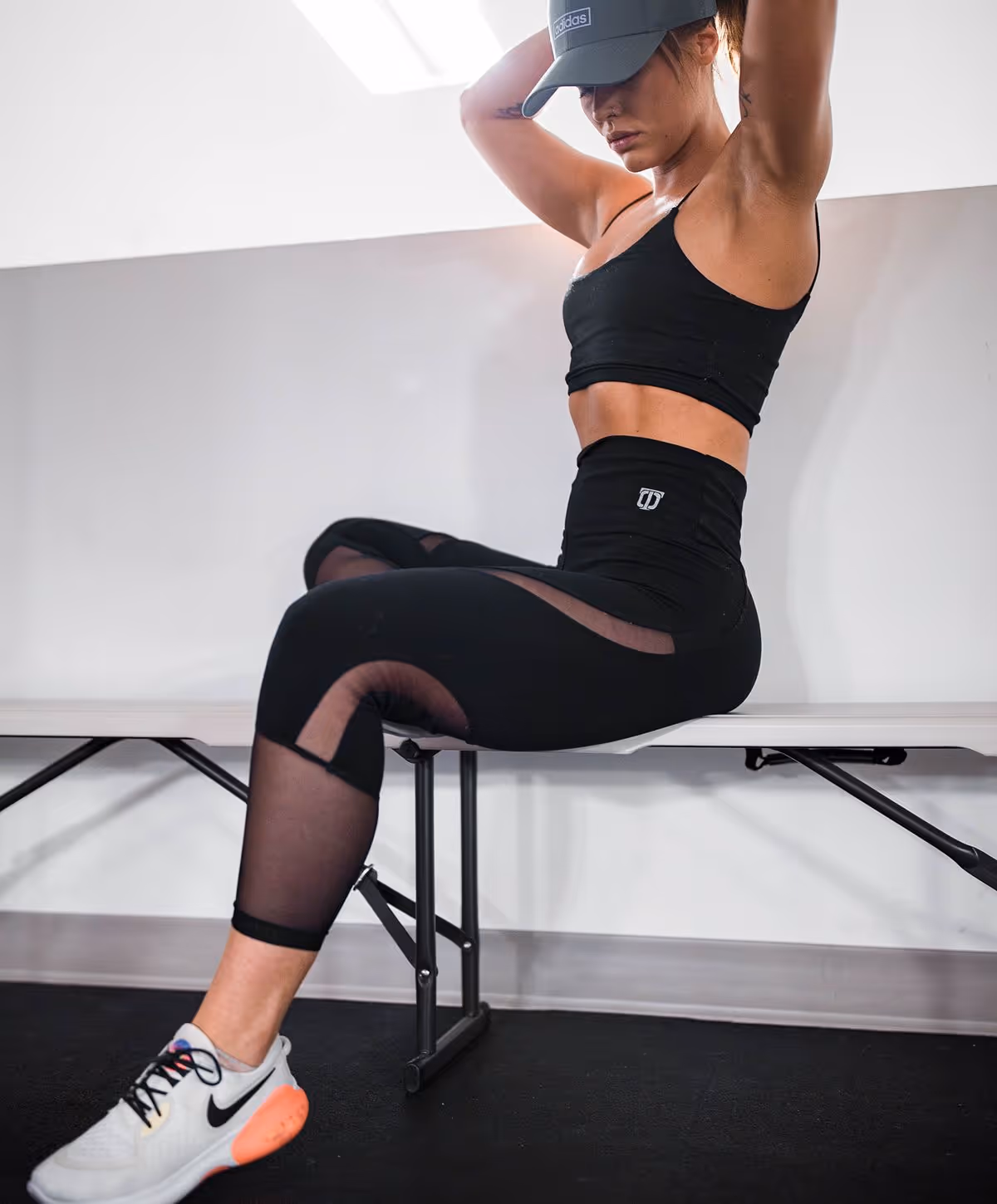 A woman wearing a black sports bra and high-waisted leggings, sitting on a bench with her hands behind her head, showcasing athletic apparel.