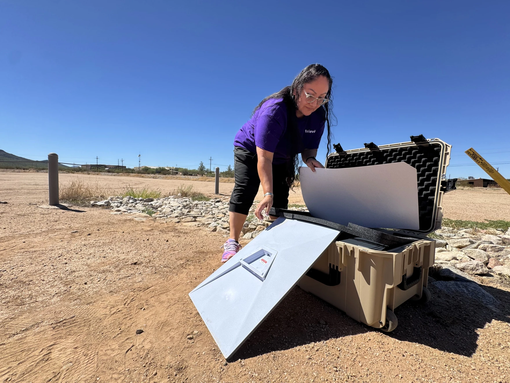 Woman in purple shirt setting up satellite equipment case in a desert