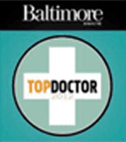 A circular logo featuring a white cross in the center, with the words 'TOP DOCTOR' in bold black and orange text, and the year '2019' below it. The top of the logo displays the word 'Baltimore' in a stylish font.