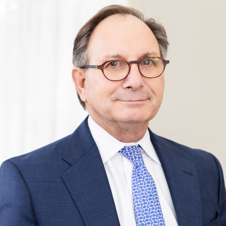 A middle-aged man with glasses wearing a blue suit and a light blue patterned tie, smiling at the camera.