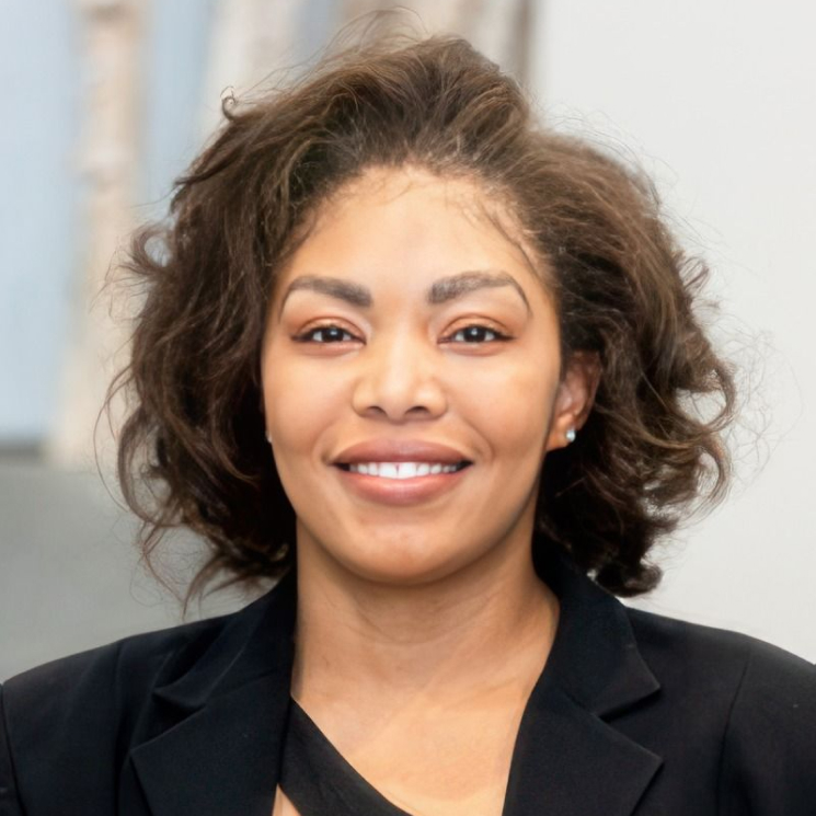 A woman with curly hair, wearing a black blazer, smiling at the camera.