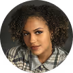 Portrait of a woman with curly dark hair in a gray plaid shirt against a dark background.