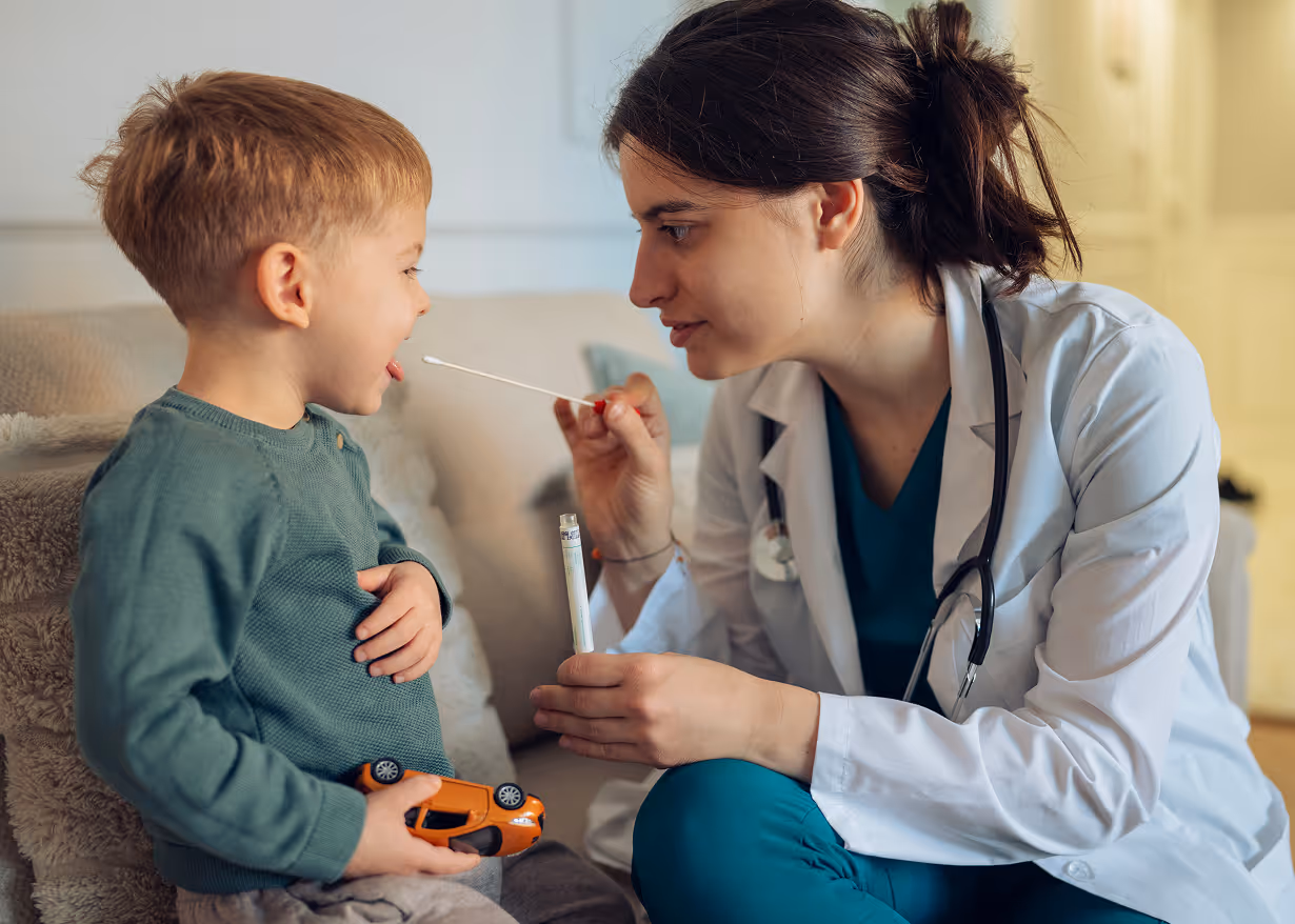 Female doctor using a swab to test a young boy sitting on a couch holding a toy car.