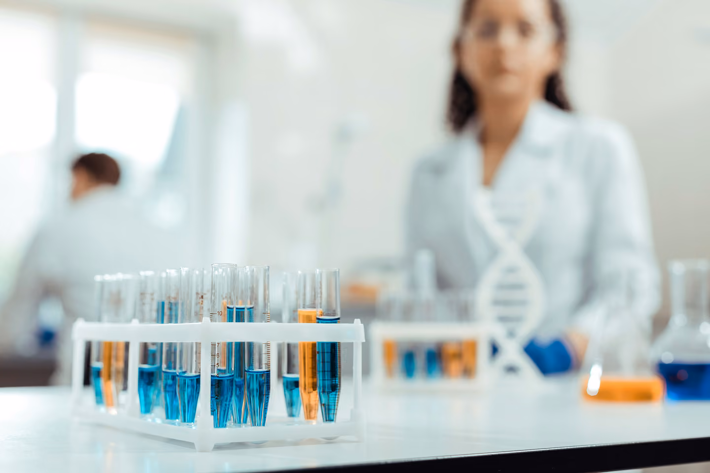 Test tubes with blue and orange liquids in a lab setting with researchers in white coats.