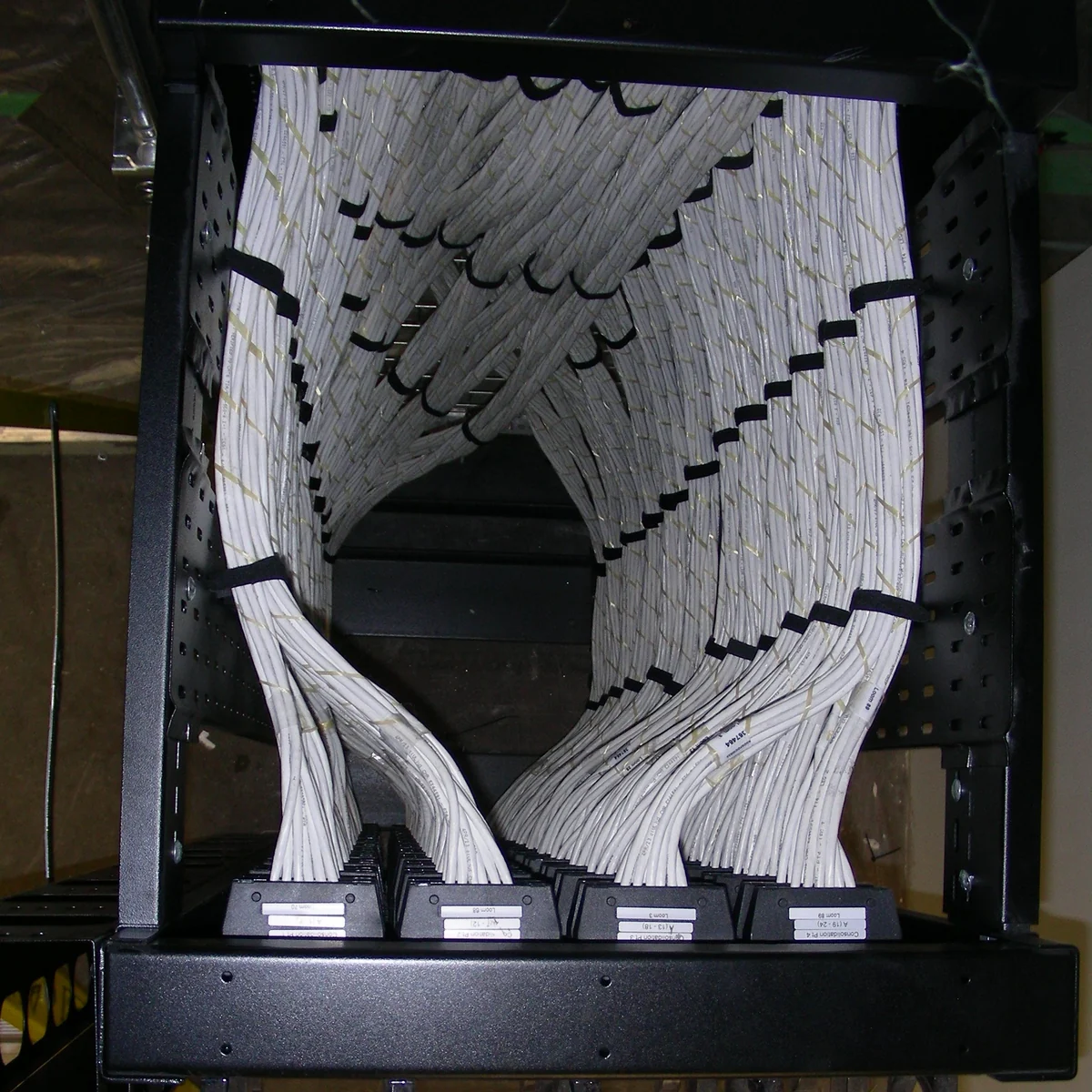The back of a prefabricated cabling assembly, white looms banded into ordered groups sweeping down into four labelled consolidation point modules