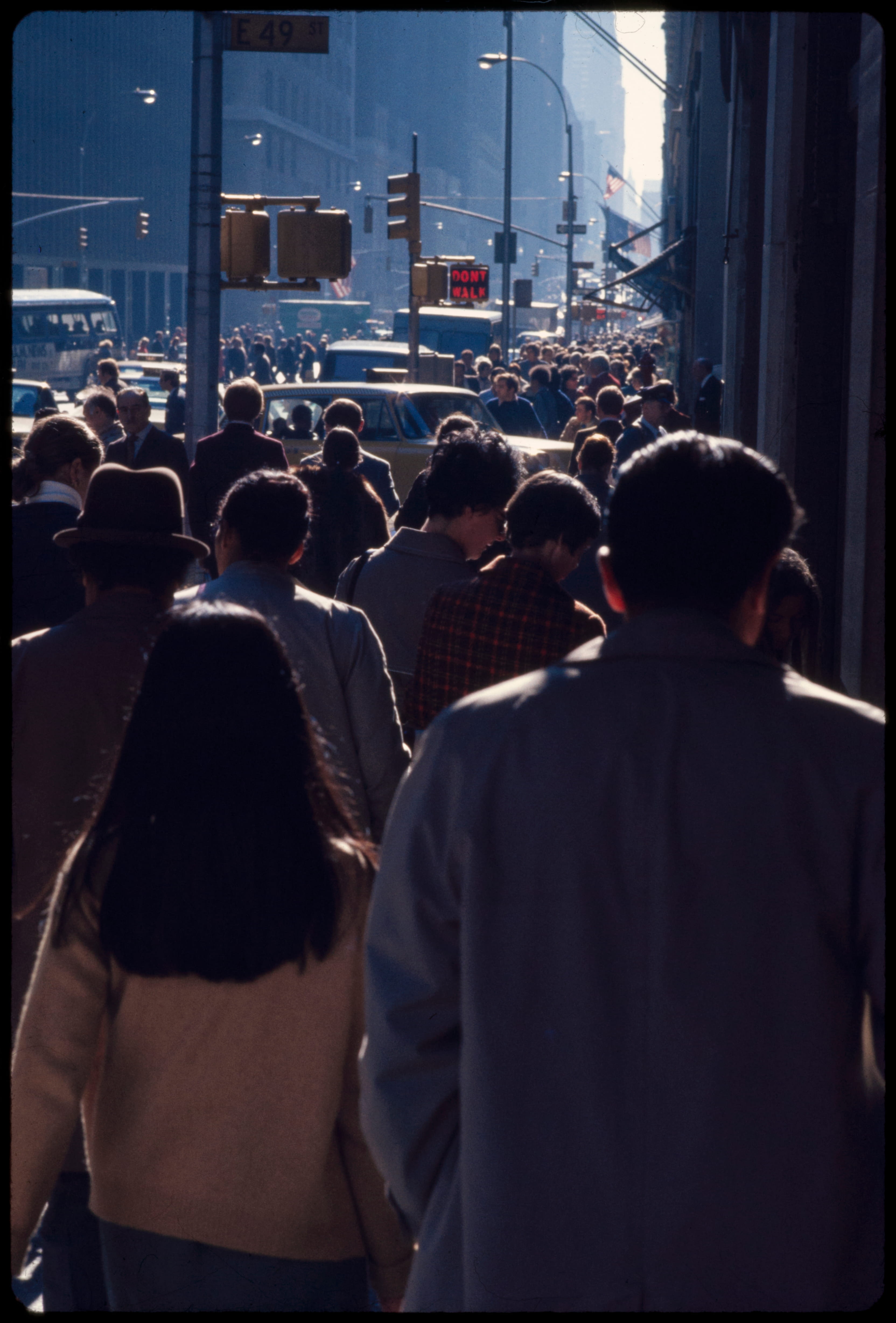 Crowded urban street filled with pedestrians and traffic under an E 49th St sign at daylight.