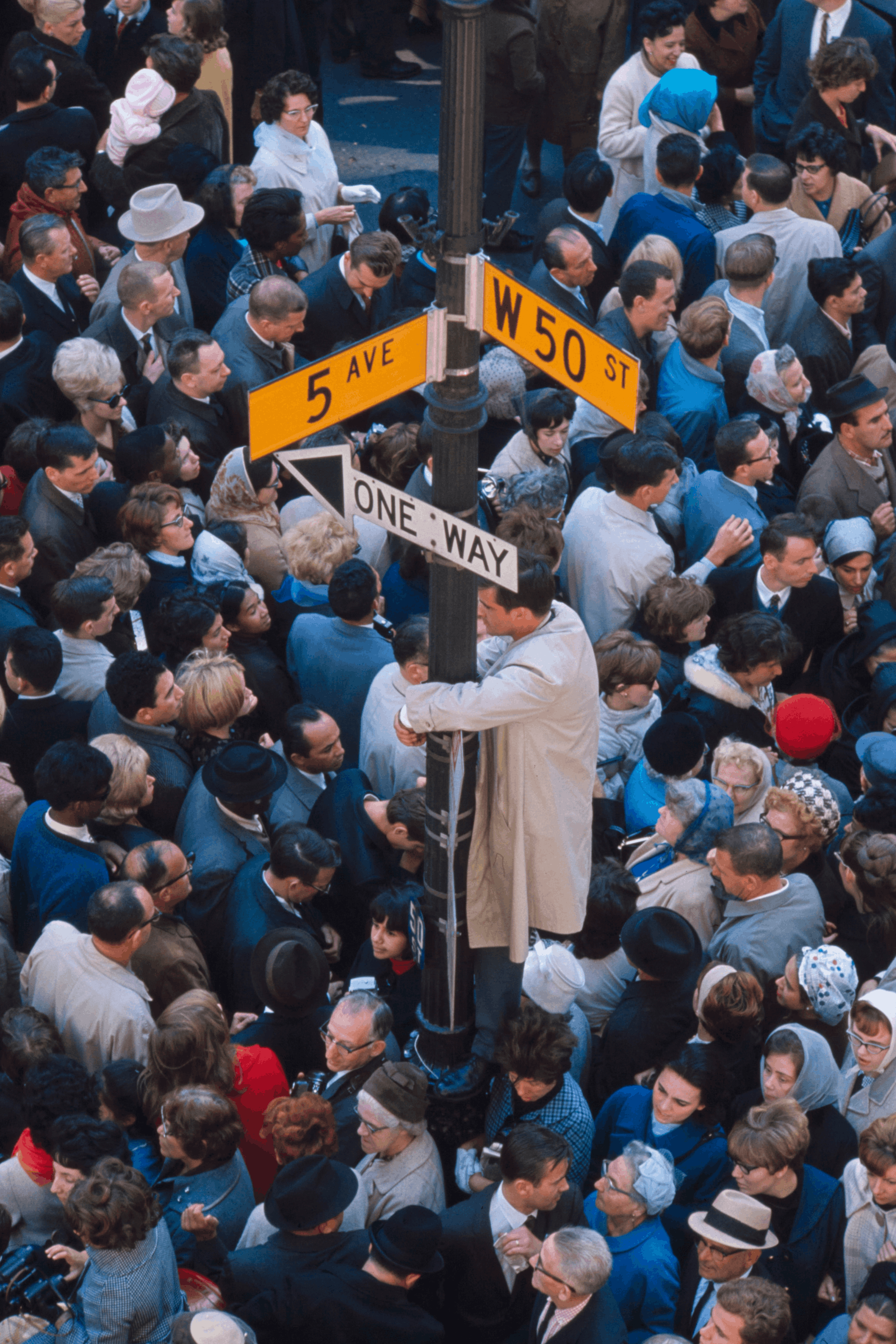 Crowd of people gathered on a street corner under signs for 5th Avenue and West 50th Street.