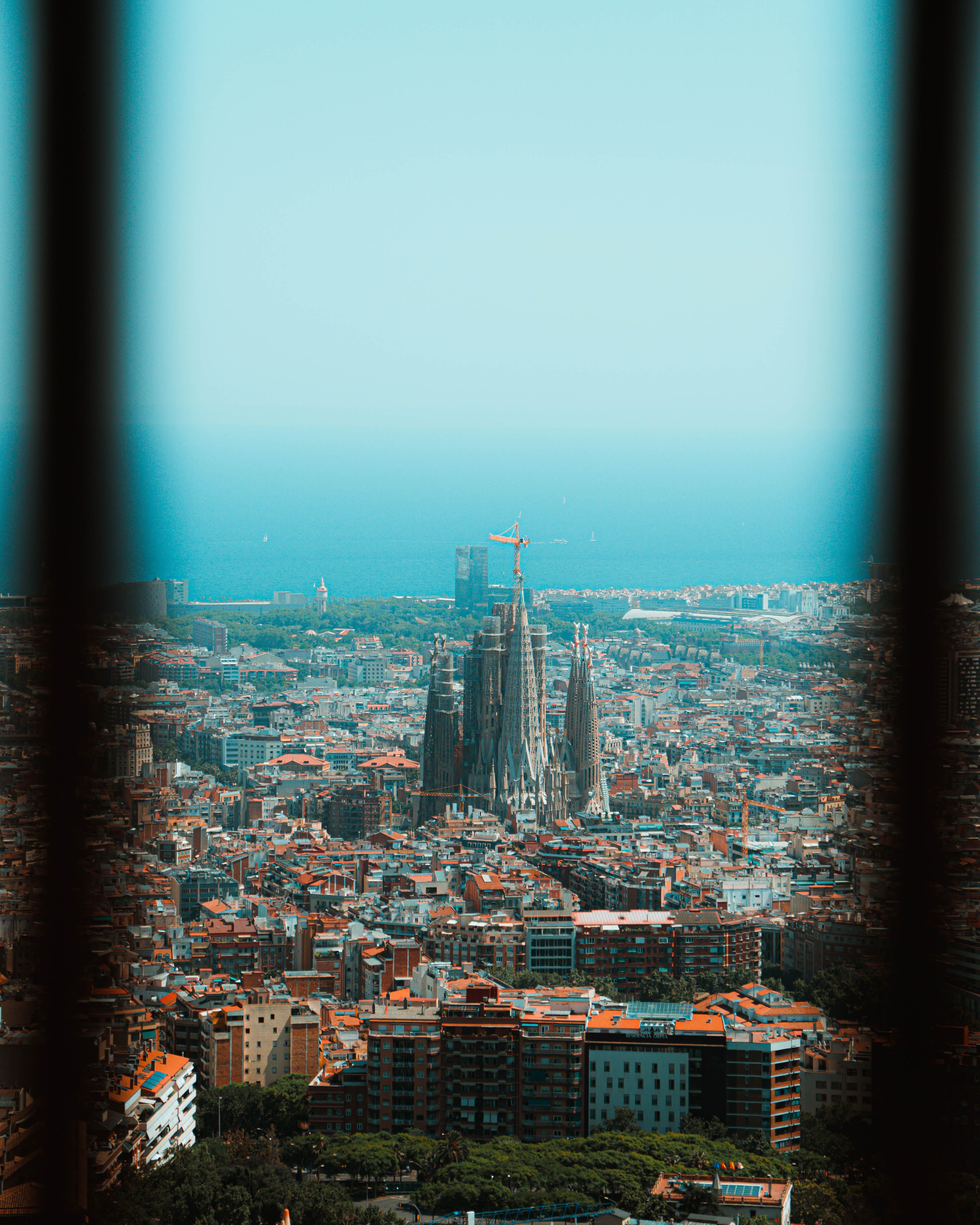 View of Barcelona cityscape with La Sagrada Familia basilica and sea in the distance between bars.