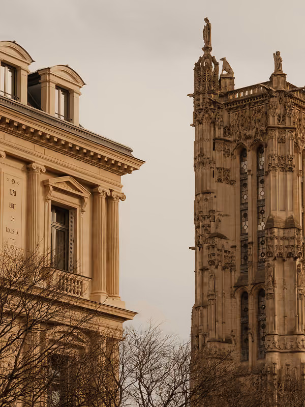 Vue de la Tour Saint-Jacques gothique à Paris à côté d'un bâtiment classique sous un ciel clair.