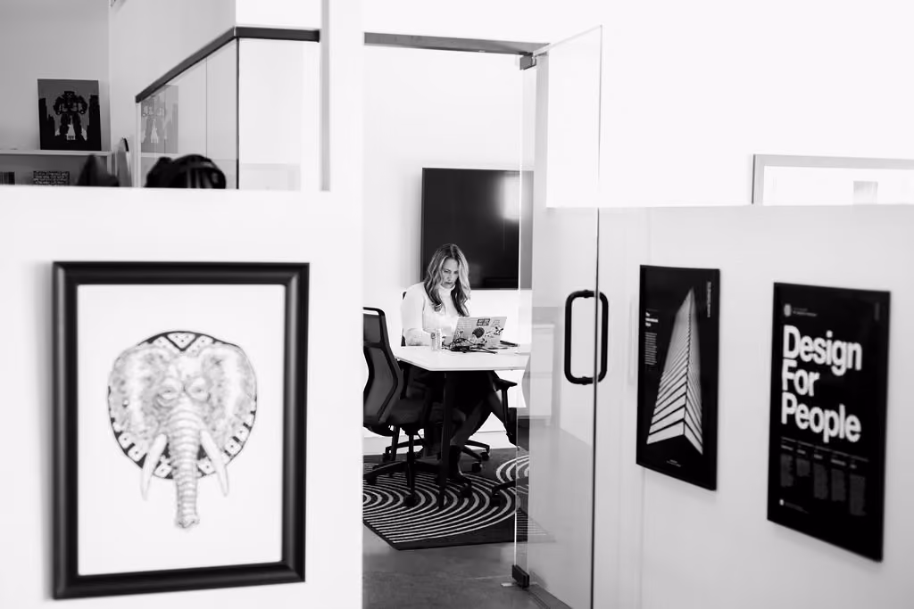 Woman working on laptop inside a modern office room with framed artwork on walls.