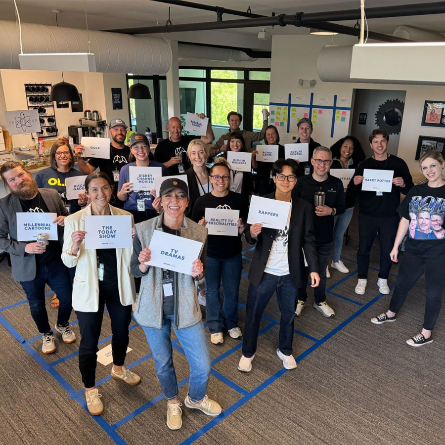 Group of people in an office holding signs with favorite TV shows, movies, and hobbies.