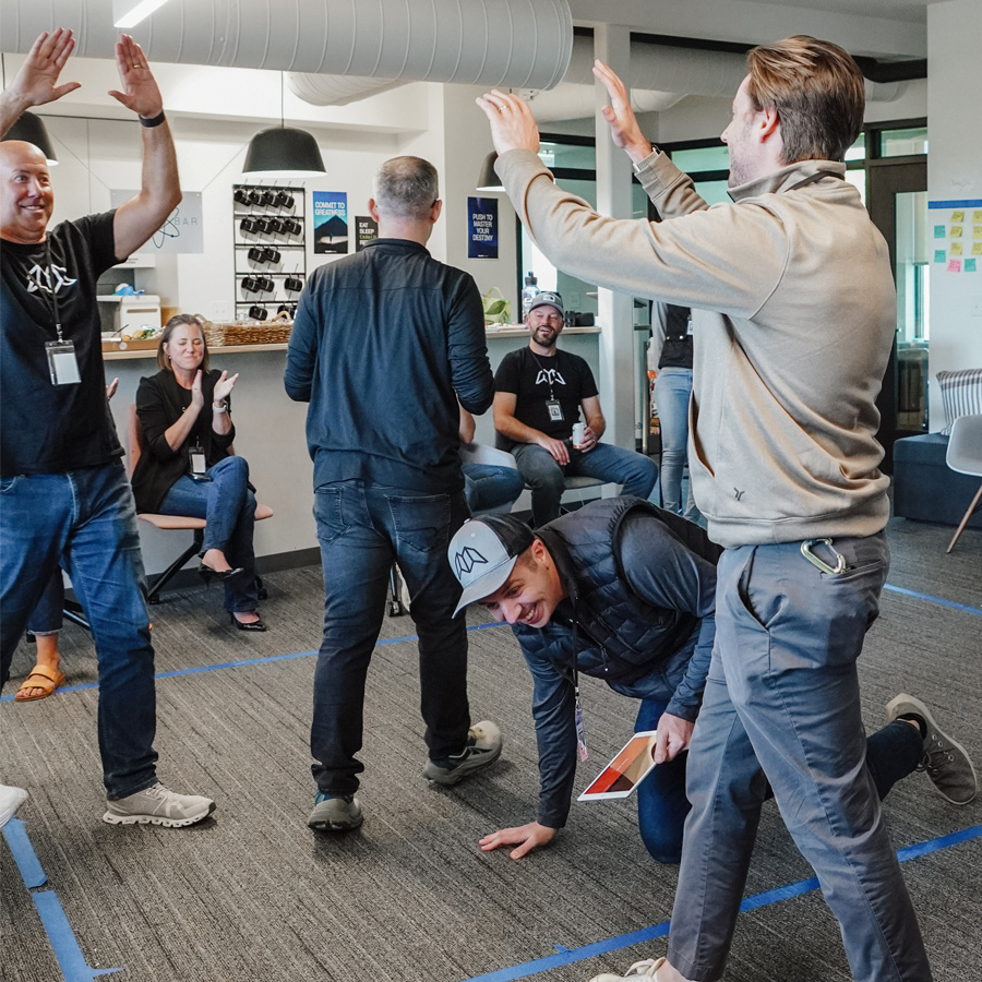 A group of coworkers laughing and celebrating inside an office with gray carpet and modern furnishings.