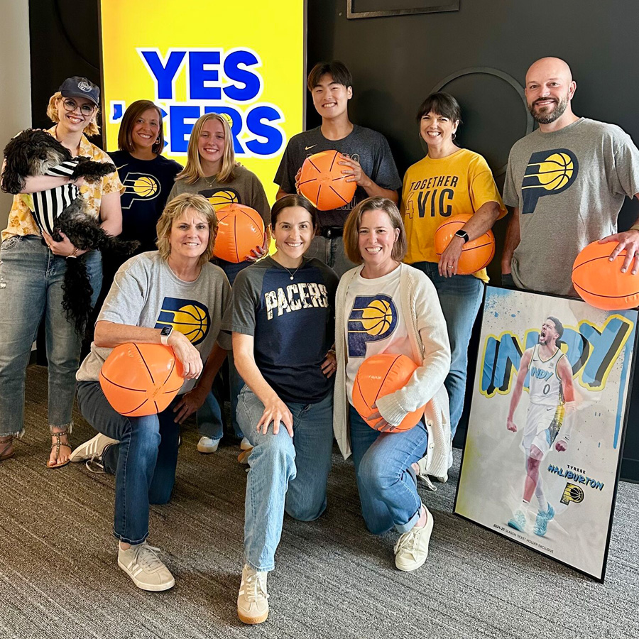 Group of people wearing Indiana Pacers shirts holding basketballs, with a dog and team sign nearby.