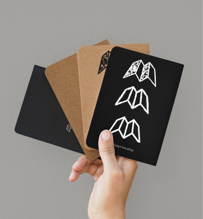 Hand holding four small notebooks with black and brown covers, one has white abstract logos.