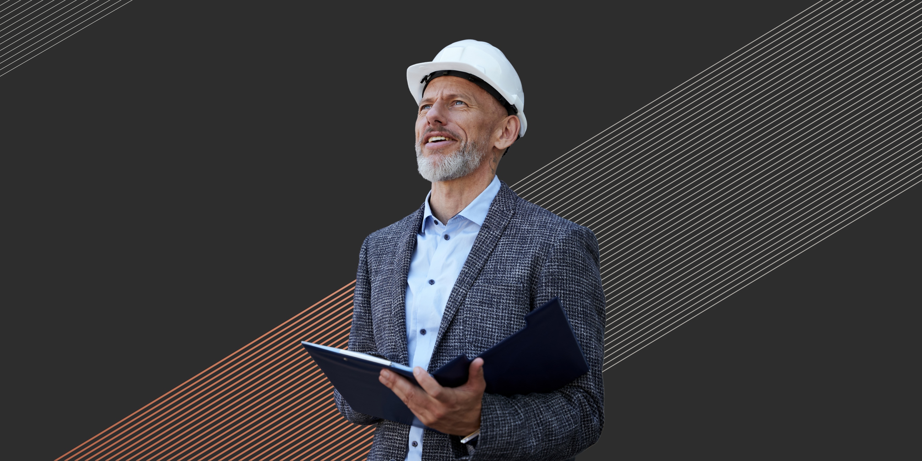 Smiling man in a white hard hat holding a clipboard, wearing a blazer and light blue shirt.