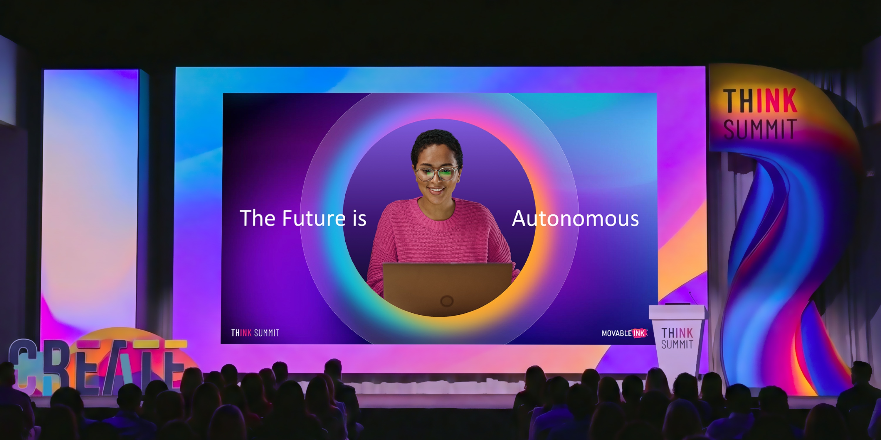 Conference stage with large screen showing a woman on laptop and text 'The Future is Autonomous'.