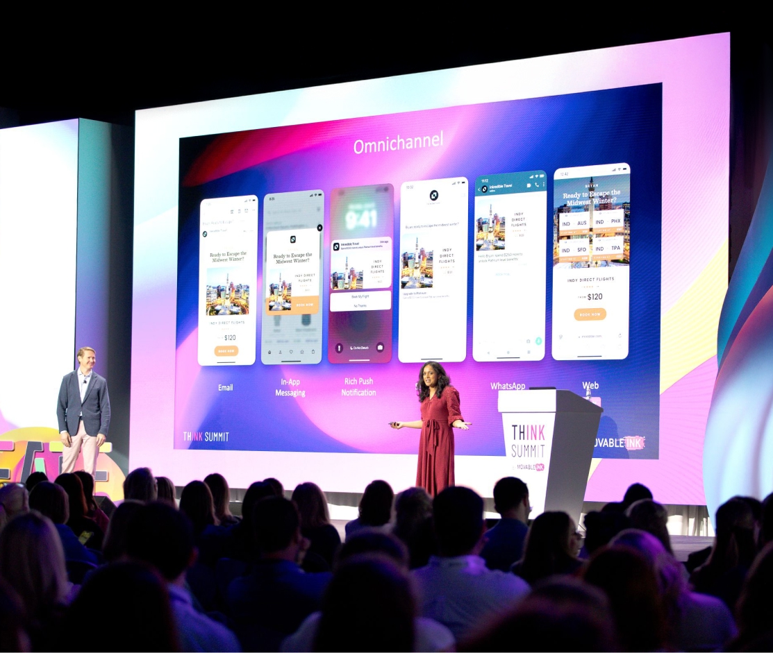 Two speakers on stage presenting omnichannel marketing with phone screens showing email, app, push, WhatsApp, and web.