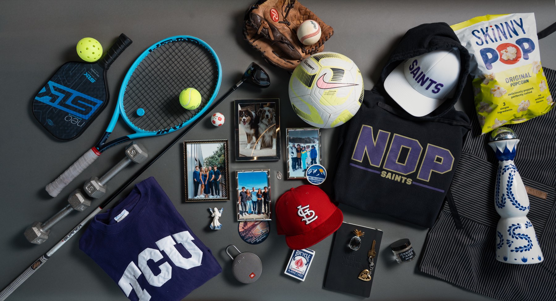 Christi Wolfe personal flatlay — sports memorabilia, photos, Cardinals cap, Saints gear, TCU, and tequila on gray background