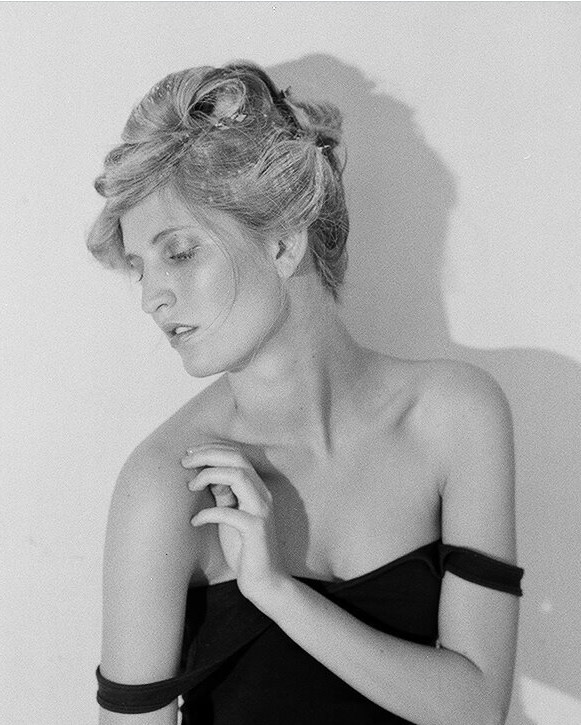 Black and white portrait of Kinsey looking down against a simple studio backdrop.