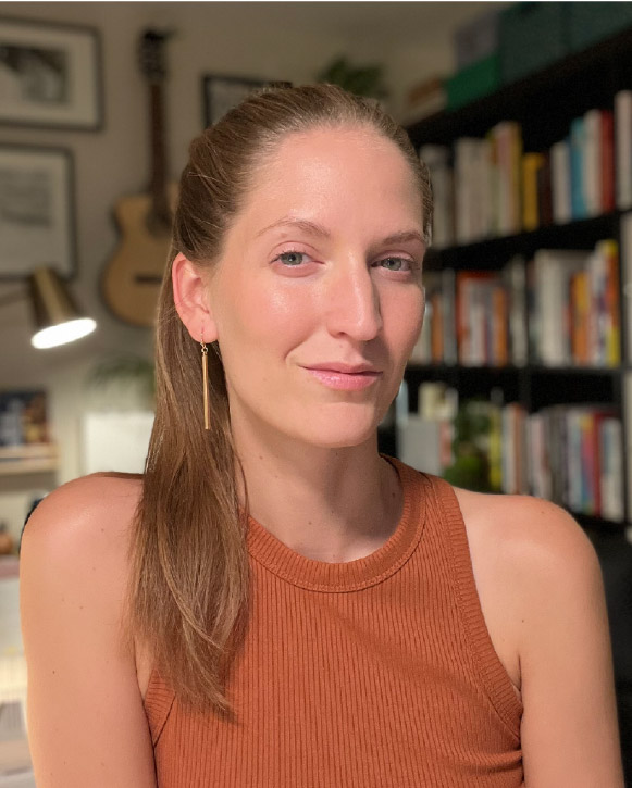 Kinsey seated indoors with bookshelves in the background.