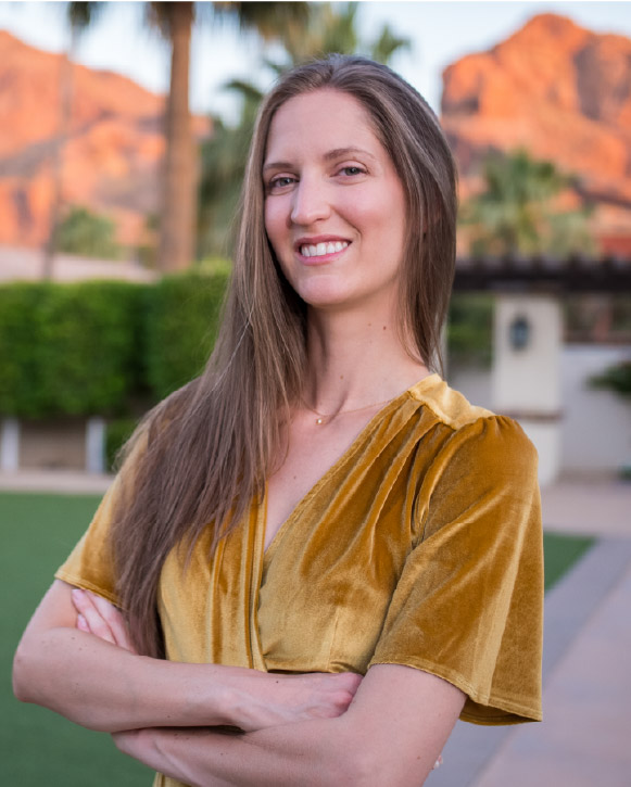 Kinsey standing outdoors in a gold top with mountains in the background.