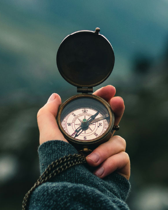 A hand holding an open compass outdoors.