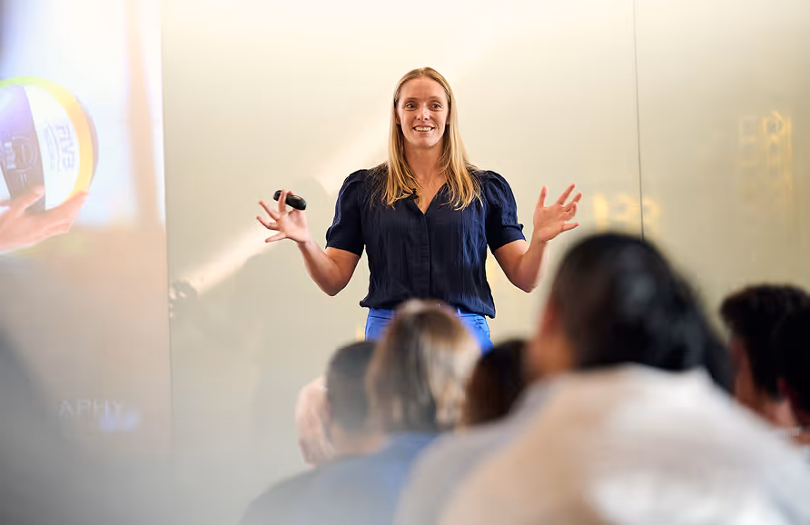 Woman speaking energetically in front of an audience during a presentation or lecture.