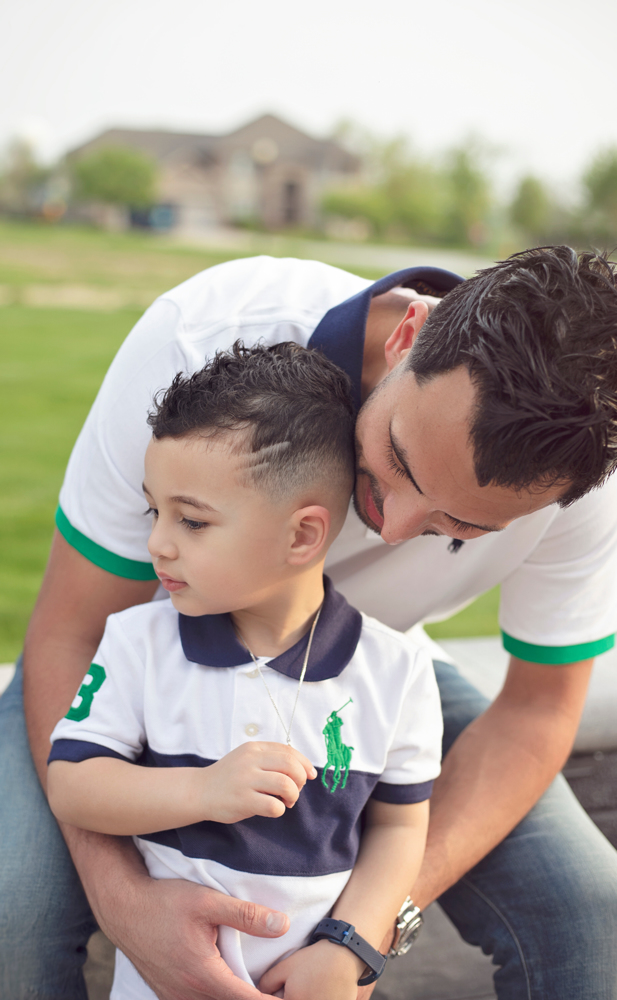 Firas Isa kissing his son Adriyan Isa on the head outdoors.