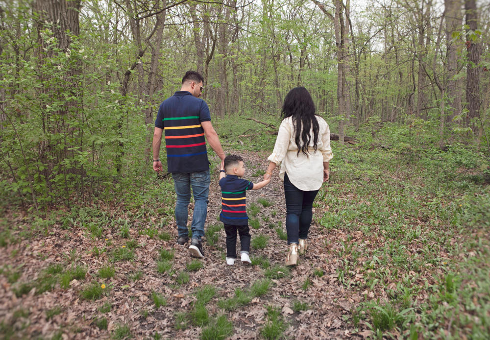 Firas Isa, Sabreen Rihan, and Adriyan Isa walking away hand in hand along a wooded path.