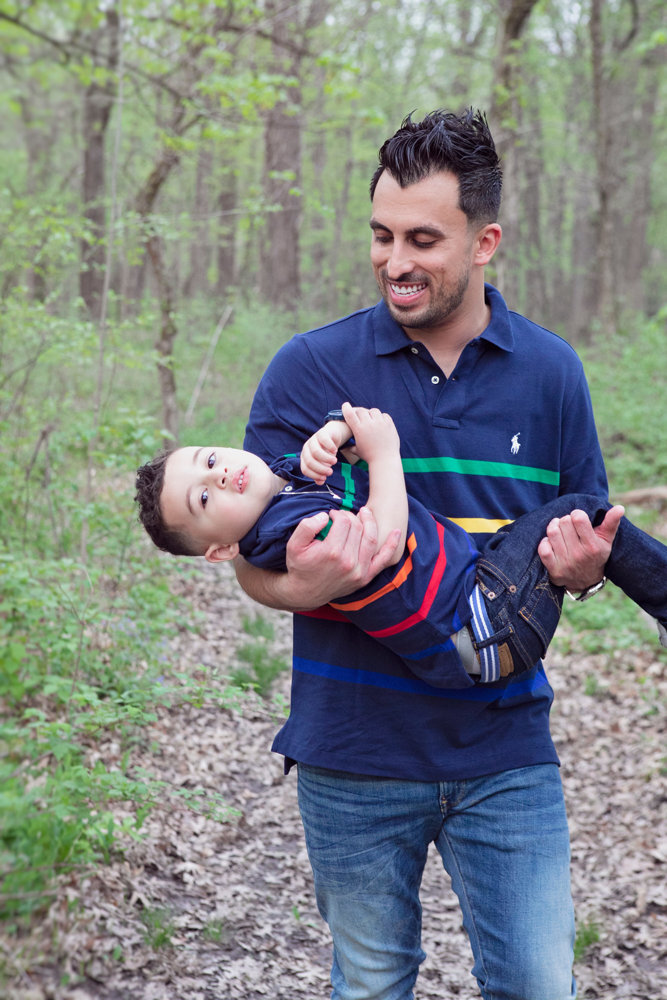 Firas Isa smiling while holding his son Adriyan Isa in his arms in the woods.