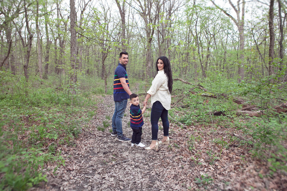 Firas Isa, Sabreen Rihan, and their son Adriyan Isa standing together on a wooded path.
