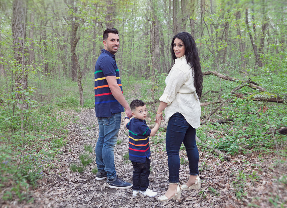 Firas Isa, Sabreen Rihan, and their son Adriyan Isa standing together on a wooded path.