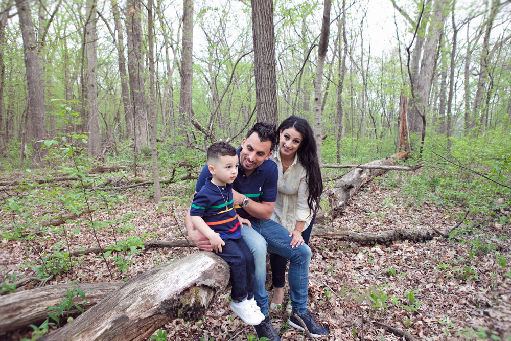 Firas Isa and Sabreen Rihan leaning close to their son Adriyan Isa on a wooded path.
