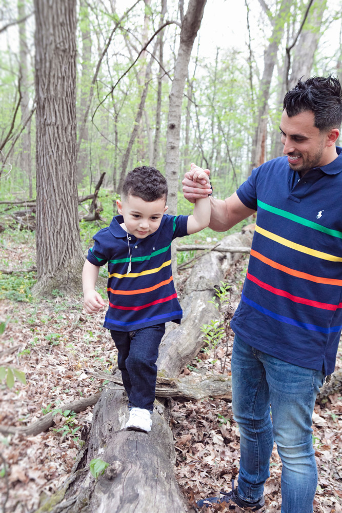 Firas Isa holding his son Adriyan Isa’s hand as Adriyan balances on a fallen log.