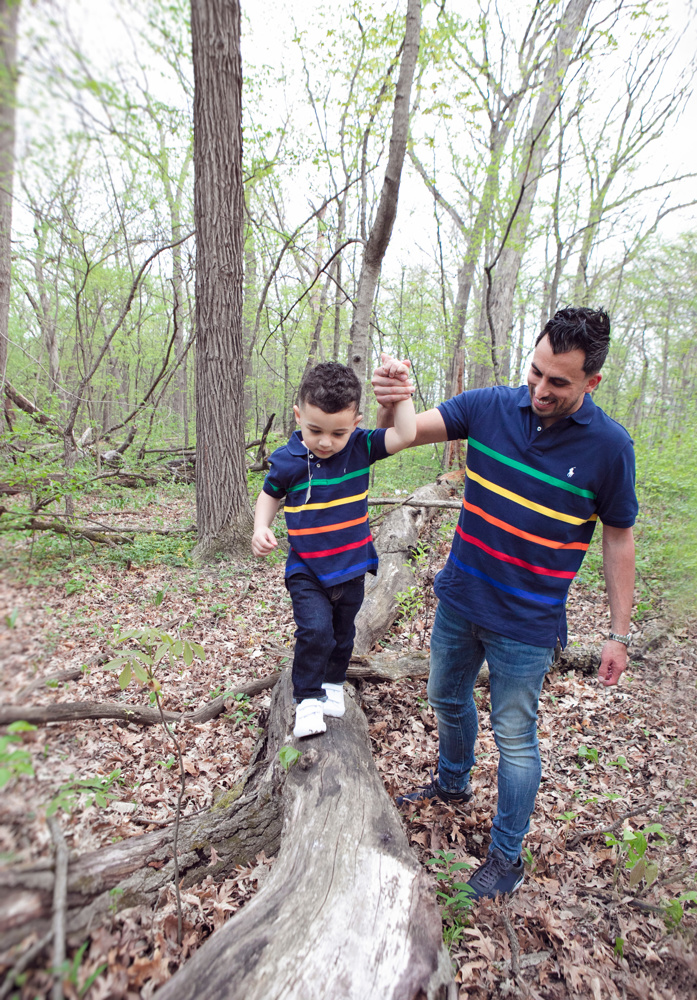Firas Isa holding his son Adriyan Isa’s hand as Adriyan balances on a fallen log.