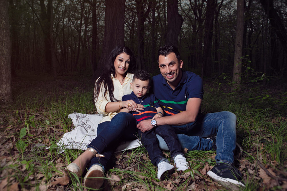 Firas Isa and Sabreen Rihan sitting together in the woods with their son Adriyan Isa.