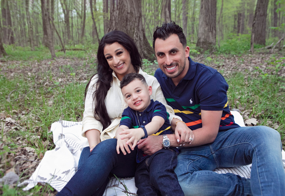 Firas Isa and Sabreen Rihan sitting together in the woods with their son Adriyan Isa.