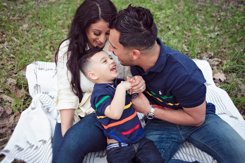 Firas Isa and Sabreen Rihan kissing their son Adriyan Isa while seated together in the woods.