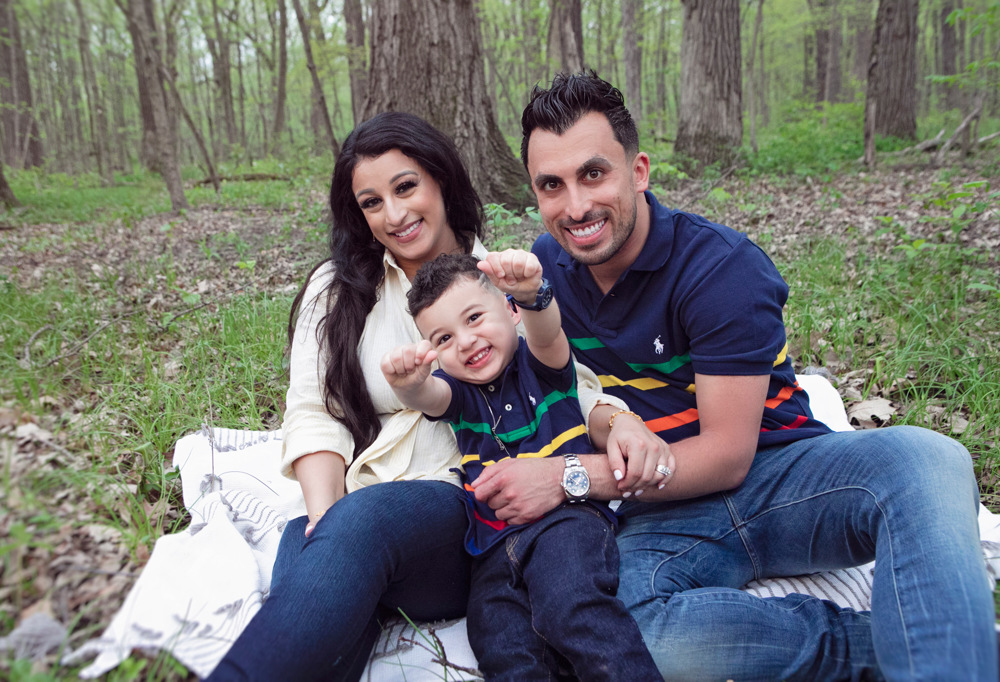 Firas Isa and Sabreen Rihan sitting together in the woods with their son Adriyan Isa.
