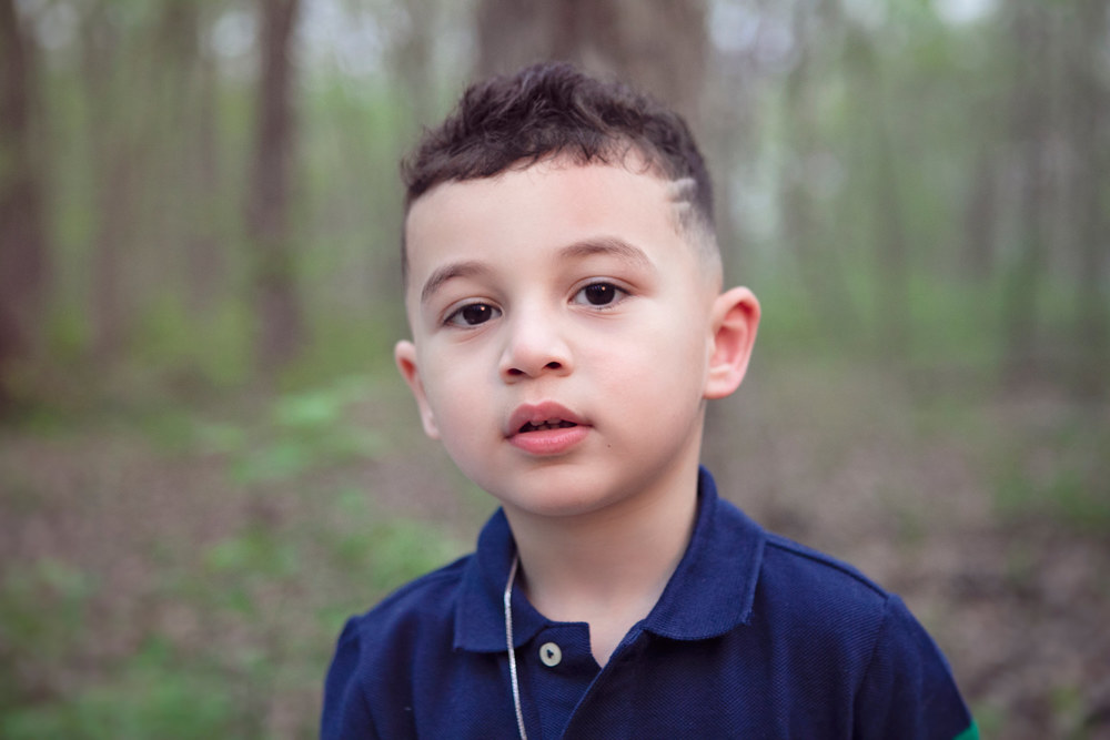 A portrait of Adriyan Isa outdoors against a softly blurred wooded background.