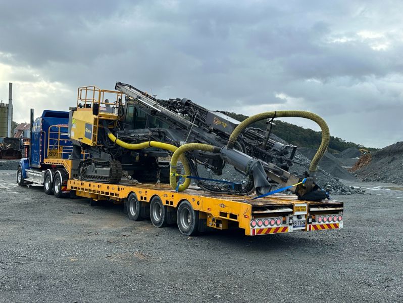 Heavy machinery with yellow hoses loaded on a yellow flatbed trailer attached to a blue truck.