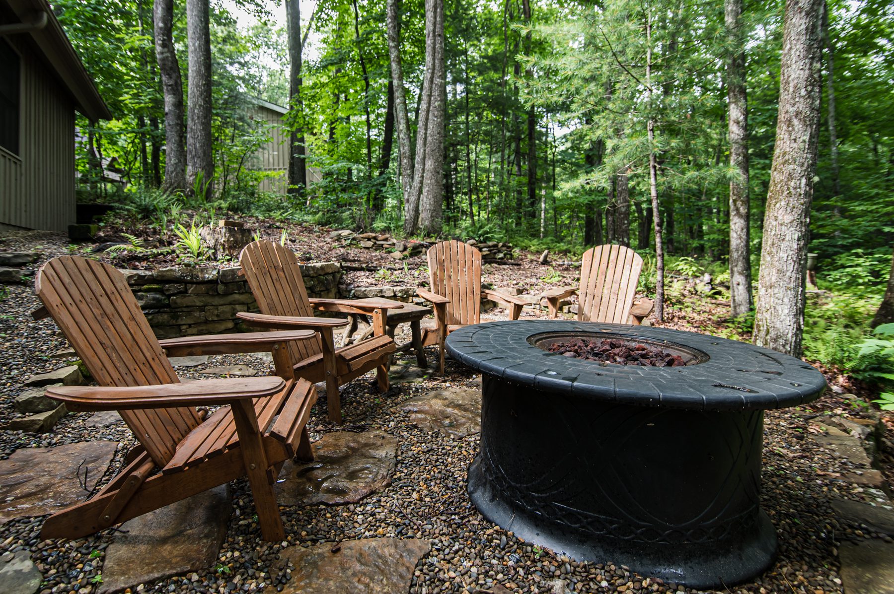 Back patio firepit with four Adirondack chairs on a stone-and-gravel terrace in the woods