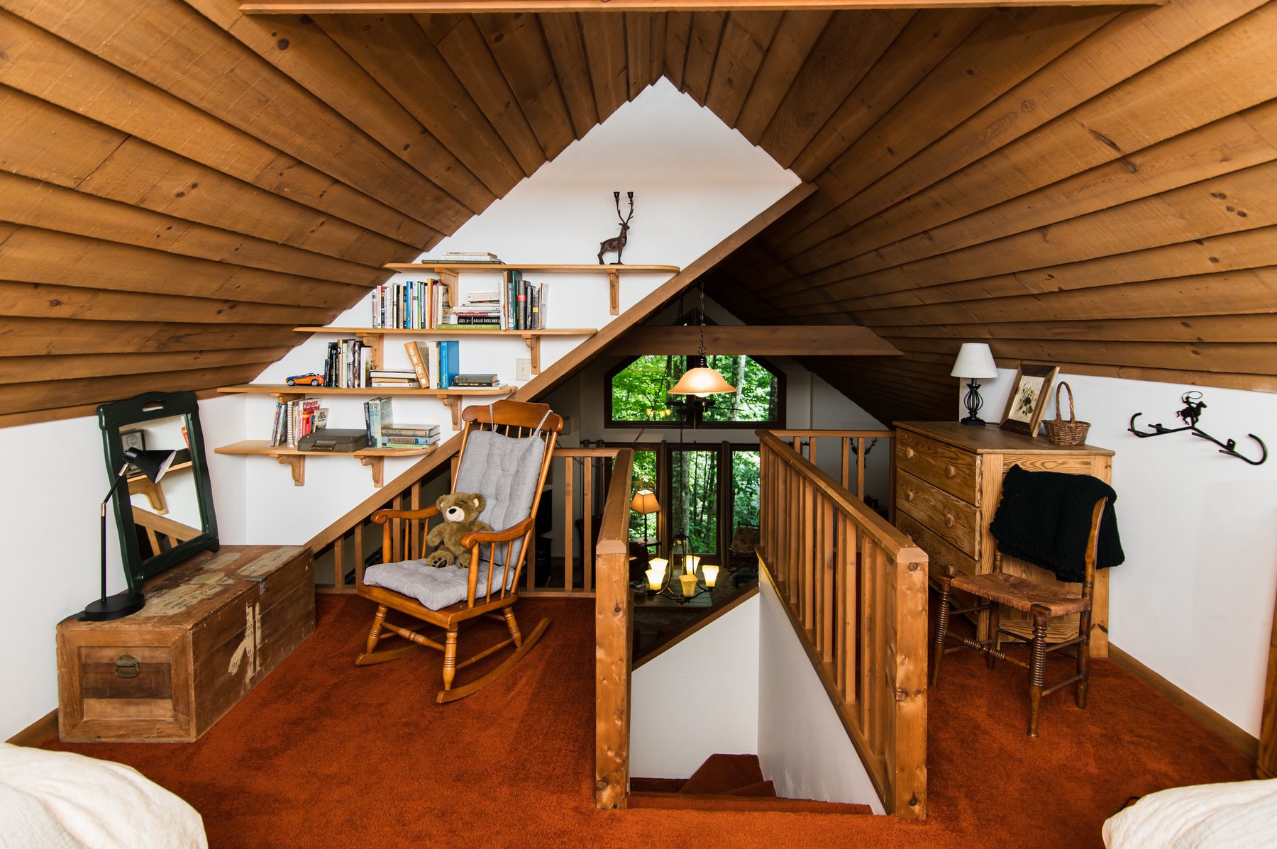 Wood-paneled sleeping loft with bookshelves, rocking chair and forest views at The Woodland Cottage