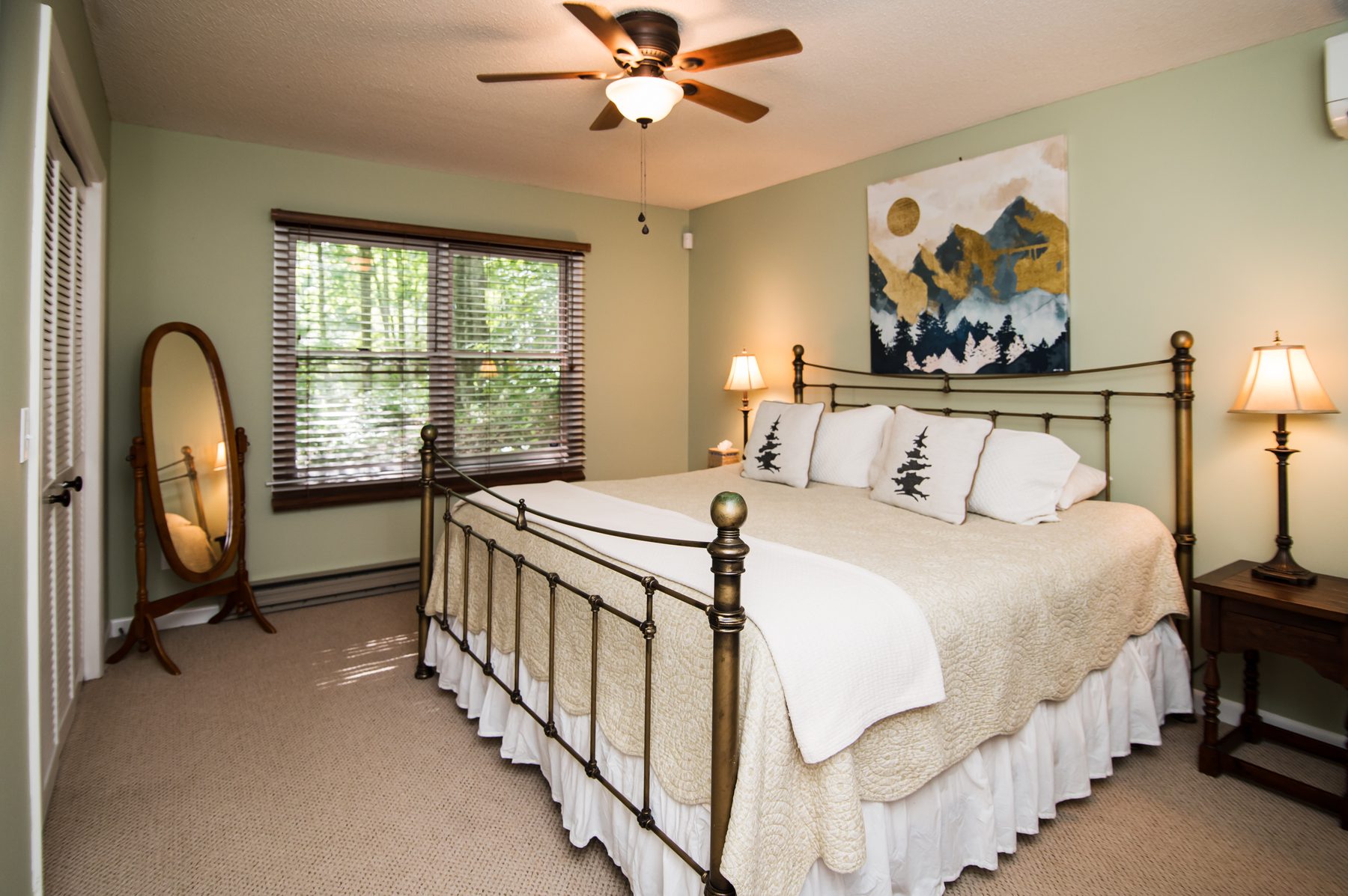 Bedroom with a king brass bed, mountain artwork and forest-view windows
