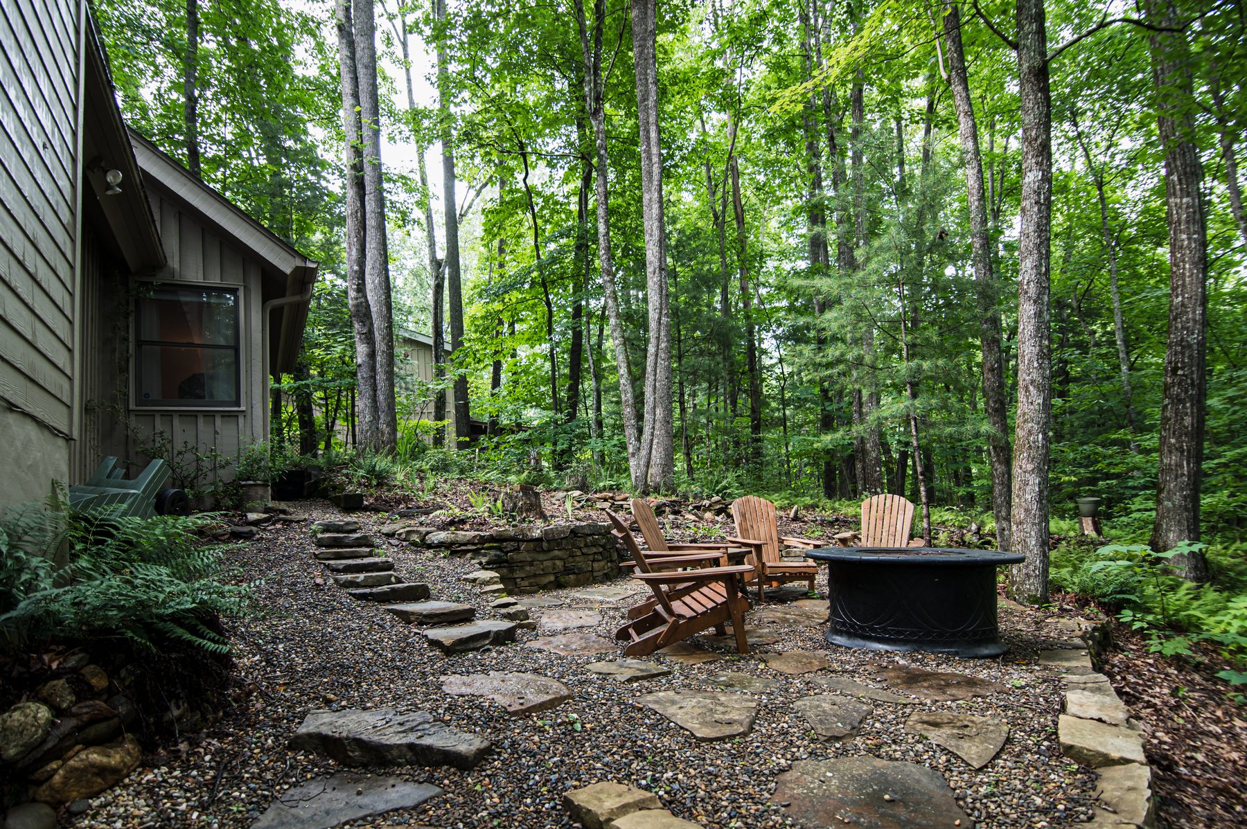 Stone-and-gravel firepit area with Adirondack chairs in the forest beside the cottage