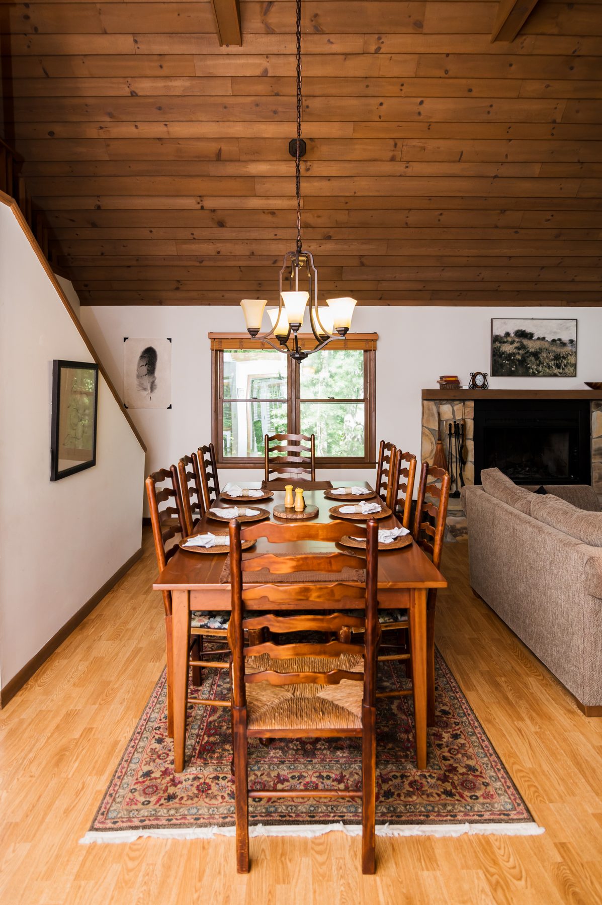 Dining table set for eight beneath a wood-plank cathedral ceiling beside the stone fireplace