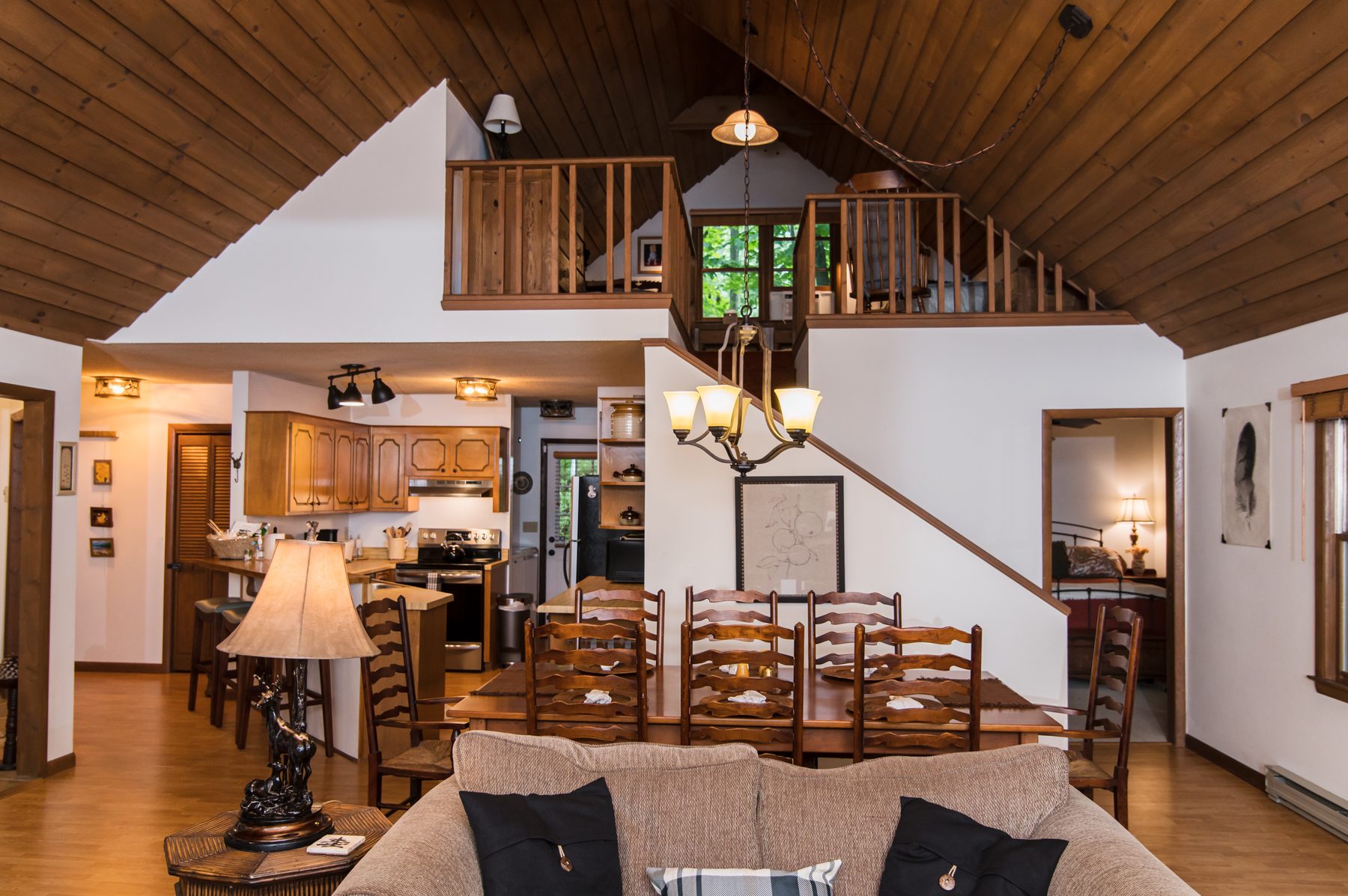 Open-plan great room with vaulted wood ceiling, dining area and loft above at The Woodland Cottage