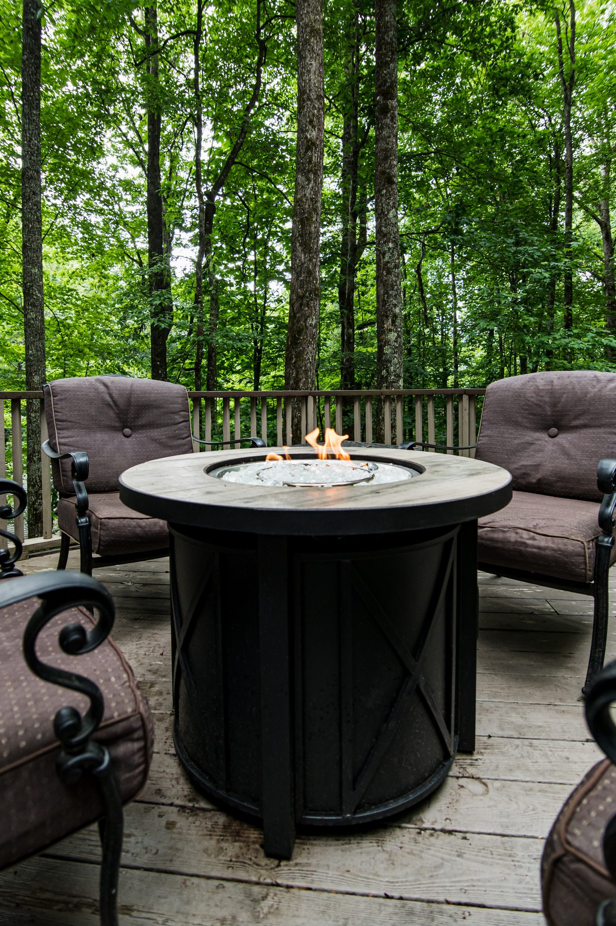 Lit gas firepit table ringed by cushioned chairs on the forest deck